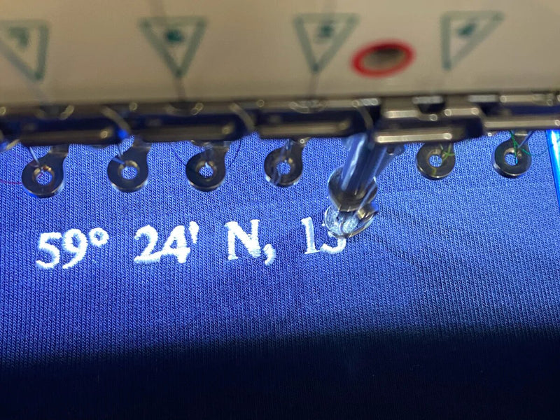blauer Sweater unter der Stickmaschine während des Stickvorgangs von oben fotografiert